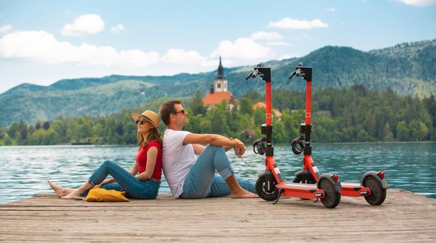 Young couple using electric scooter as modern ecological mean of transport while exploring green country Slovenia at vacations. Green eco energy concept with zero emission. Warm sunshine filter