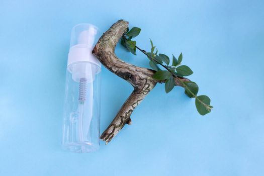 Cosmetic liquid product in a bottle with a dispenser and an old wooden snag on a blue background. The concept of beauty skin care.