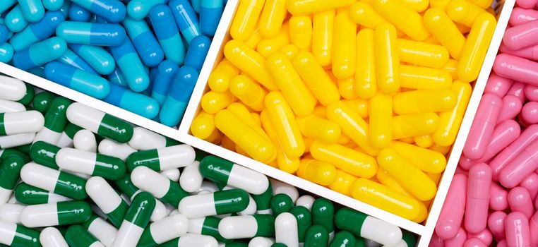Top view of colorful capsule pills in plastic box. Pink, yellow, blue, green-white capsule pills in tray. Pharmacy web banner. Pharmaceutical industry. Healthcare background. Online pharmacy concept.