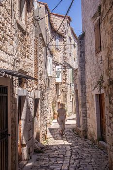 Rear view of beautiful blonde young female traveler wearing straw sun hat sightseeing and enjoying summer vacation in an old traditional costal town at Adriatic cost, Croatia.