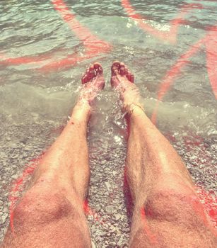 Legs are cooling in water. Bare feet in water close to to lake bank.  Abstract.