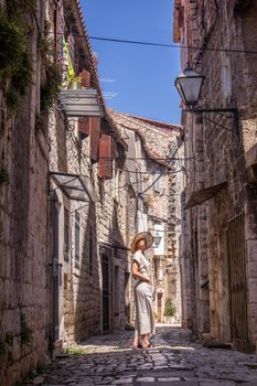 Beautiful blonde young female traveler wearing straw sun hat sightseeing and enjoying summer vacation in an old traditional costal town at Adriatic cost, Croatia.