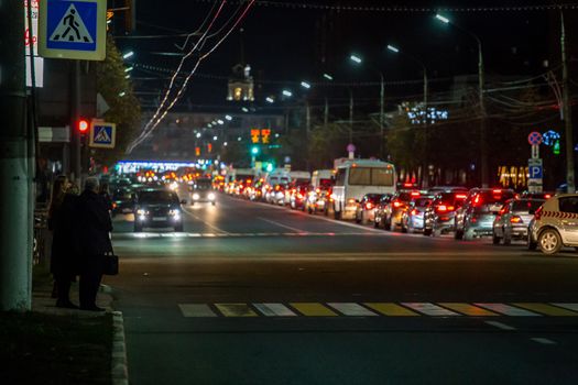 TULA, RUSSIA - OCTOBER 16, 2018: citizens waiting signal for crossing central prospect at night in light of traffic with blurry background jam