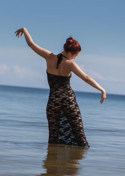 Young red-haired woman in a black lace dress on a naked body posing on the seashore