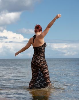 Young red-haired woman in a black lace dress on a naked body posing on the seashore