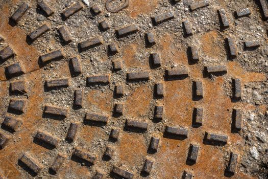 Rusty sewer manhole cover. Geometric pattern on the cover of the sewer manhole. Close-up view of the texture of the old rusty metal sewer manhole.