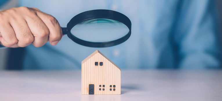 Hand of businessman hold magnifying glass looking house for examining and analyzing quality, inspection and check home, purchase and search residential and investment, business and property concept.