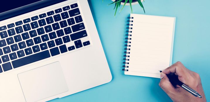 Flat lay, hand of businessman writing on notebook with Laptop computer and plant and pen on desk in office, workplace and notebook and potted tree and book, top view, business concept.