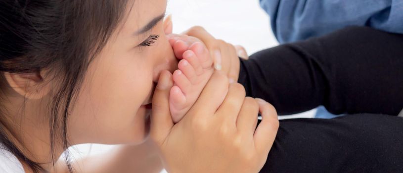 Young asian mother kiss foot of little baby girl on bed in bedroom at home, mom and newborn with relationship and bonding together, motherhood with love and care child with happy, family concept.