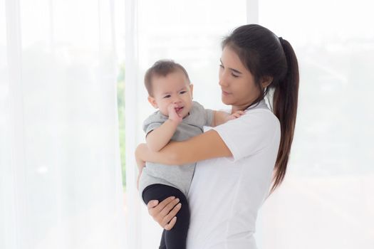 Young asian mother holding little baby girl and walking together in the bedroom at home, mom carry daughter and care, relationship of parent and child, toddler and parent, indoor, family concept.