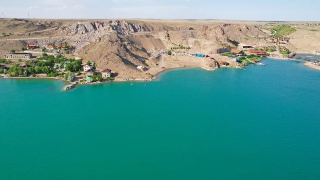 A group of people ride sup surfing in the lake. Aerial view from the drone of the green water and rocky beaches. Inflatable sapboard board. Trees and bushes grow on the bank of Kapchagai.