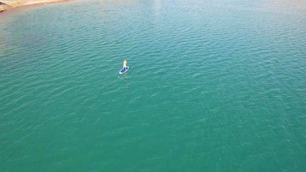 A group of people ride sup surfing in the lake. Aerial view from the drone of the green water and rocky beaches. Inflatable sapboard board. Trees and bushes grow on the bank of Kapchagai.