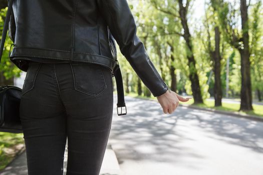 girl in black jacket and jeans stops the car on sunny day. back view