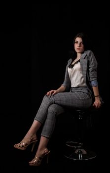 young beautiful girl in a business suit posing sitting on chair in studio on black background
