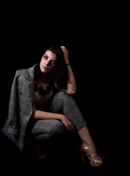 young beautiful girl in a business suit posing sitting on floor the studio on black background