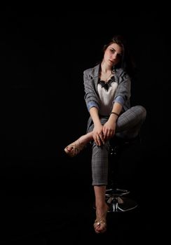 young beautiful girl in a business suit posing sitting on chair in studio on black background