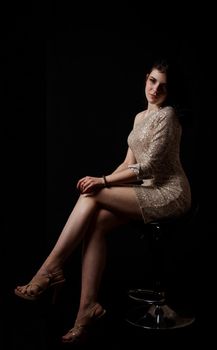young beautiful brunette girl in bright dress posing sitting on chair in the studio on black background