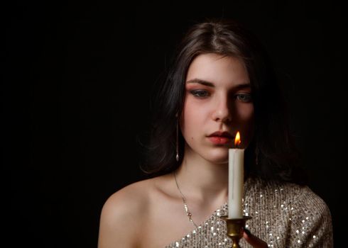 young beautiful brunette girl in bright dress holding burning candle in studio on black background