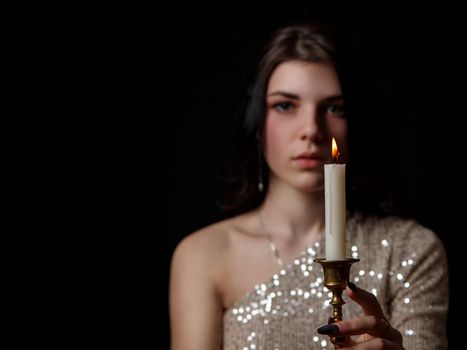 young beautiful brunette girl in bright dress holding burning candle in studio on black background