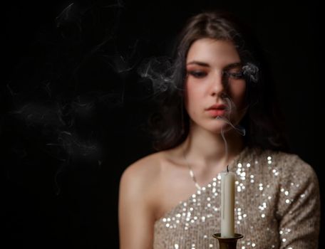 young beautiful brunette girl in bright dress holding candle in studio on black background