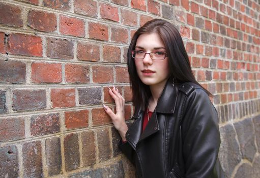 young beautiful girl in black jacket and jeans stands near the old fortress wall on sunny day. closeup outdoor