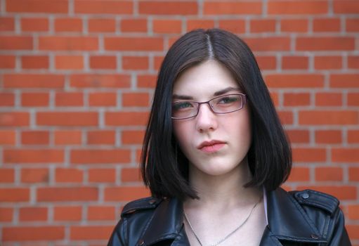 portrait of young beautiful brunette disgruntled girl near brick wall. closeup outdoor