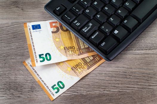 50 euro bills and computer keyboard on wooden background