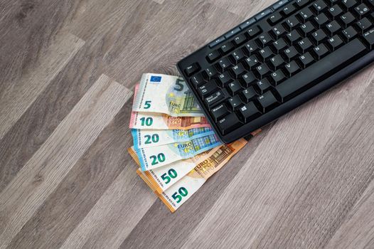 computer keyboard with euro banknotes wooden background