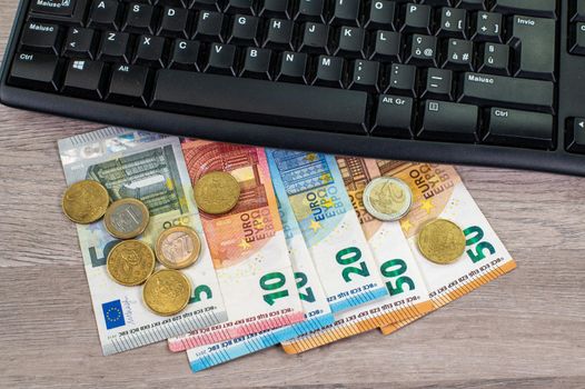 euro money of different denominations and computer keyboard on wooden background