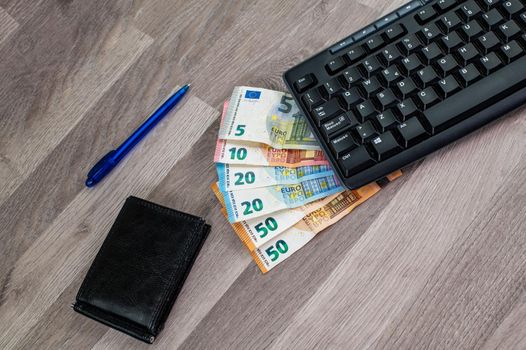 computer keyboard with euro banknotes wooden background with office items