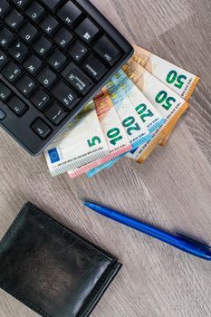 computer keyboard with euro banknotes wooden background with office items