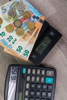 euro money of different denominations on top of a scales and calculator on wooden background