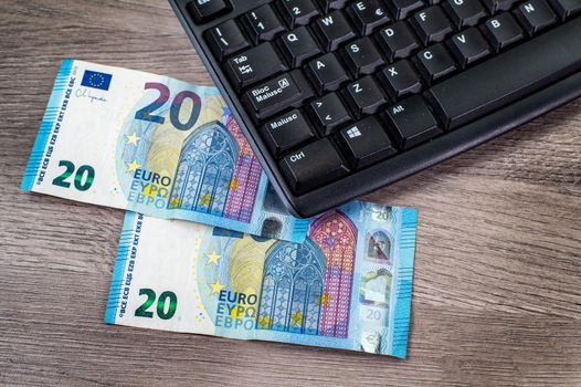 20 euro bills and computer keyboard on wooden background