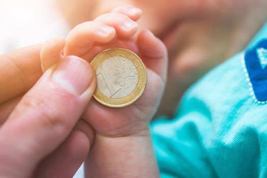 Close up of newborn baby hands holding a coin, retirement arrangement concept