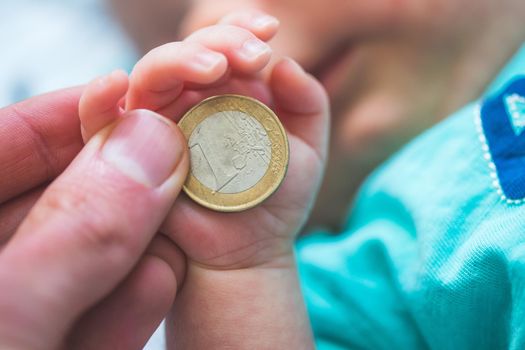 Close up of newborn baby hands holding a coin, retirement arrangement concept