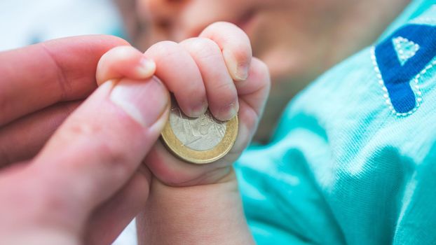 Close up of newborn baby hands holding a coin, retirement arrangement concept