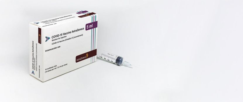 Cambridge, UK, february 5th 2021: A syringe next to the AstraZeneca Covid-19 Vaxzevria vaccine box isolated on a white background. Health and prevention. Copy space and banner
