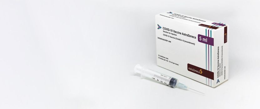 Cambridge, UK, february 5th 2021: A syringe next to the AstraZeneca Covid-19 Vaxzevria vaccine box isolated on a white background. Health and prevention. Copy space and banner