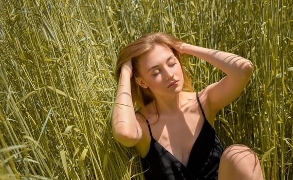 beautiful young woman sitting in the grass on the spring green field