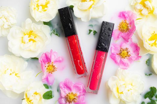 Lip gloss with flowers and water drops on a white background. The concept of a bottle of lip gloss without labels. Cosmetology. Decorative cosmetics. Copy space