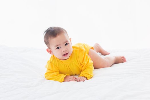 Portrait of beautiful young Asian newborn little baby prone on the bed at home, Happy baby smile wears a yellow shirt relaxing in the room, Family morning at home