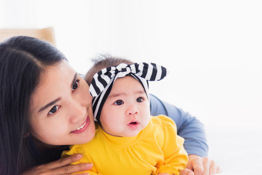 Portrait of beautiful young Asian mother playing and smiling together with his newborn little baby at home, Parent mom and little kid relaxing in the bedroom, Family having fun together