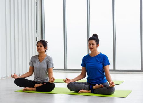 Two Asian women sporty attractive people practicing yoga lesson together, working out at the fitness GYM, Young and senior female exercising do yoga in yoga classes, sport healthy lifestyle