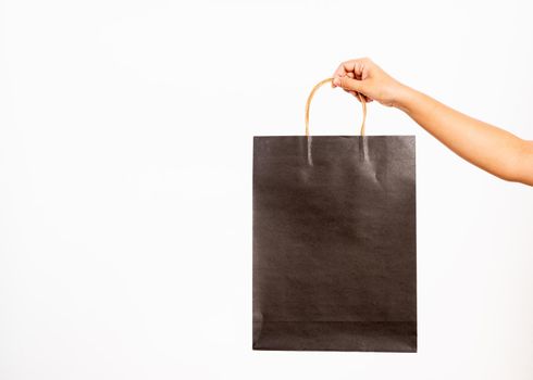 Closeup women hand holding a black shopping bag, studio shot isolated on white background, female holds in hand white clear empty blank craft paper gift bag for purchases