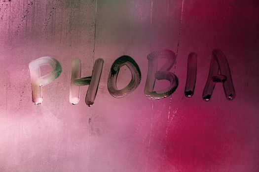 the word phobia handwritten on wet foggy window glass surface with red background light.