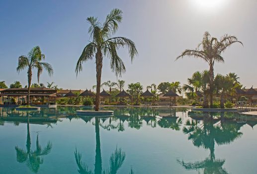 Outdoor swimming pool in a tropical luxury hotel resort with palm tree and reflection in water