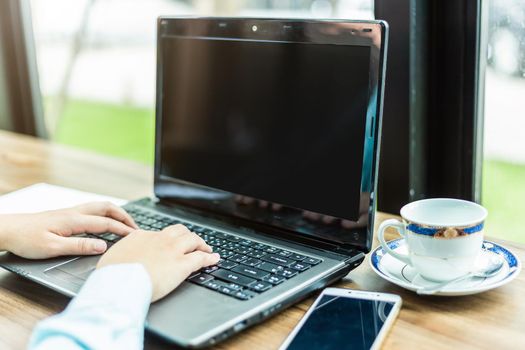 Close-up of Business woman working with smartphone,laptop with blank blank screen and document in coffee shop like the background.