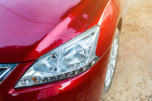 Closeup of headlight of red car outdoors.