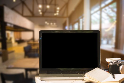 Mockup image of laptop with blank black screen with camera,notebook,coffee cup on wooden table of In the coffee shop background.