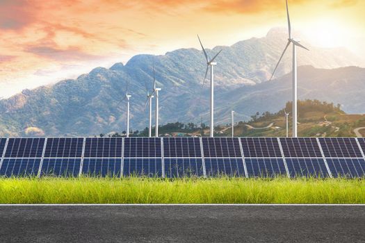 Asphalt road with solar panels with wind turbines against mountanis landscape against sunset sky,Alternative energy concept